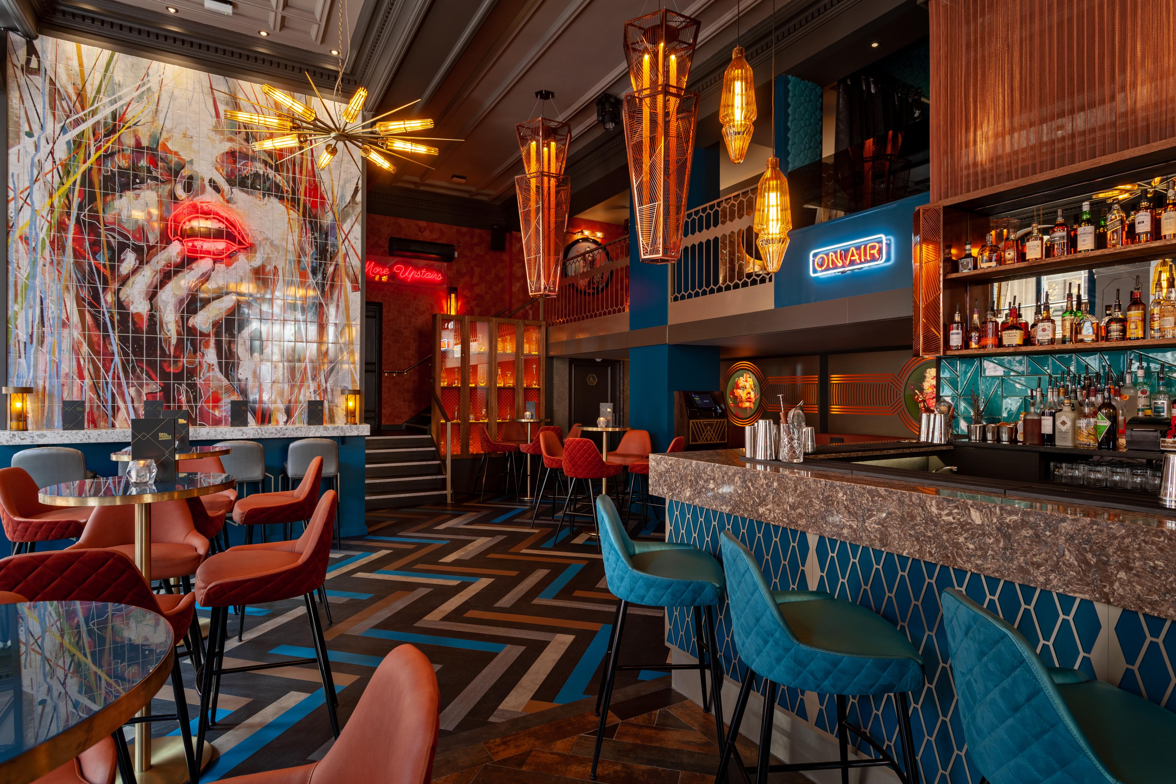 The main bar area of Dirty Martini Birmingham with large wall art, neon signs and high seating